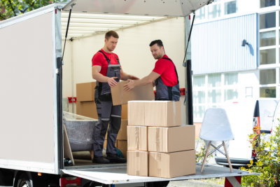 Two Young Men Unloading And Stacking The Brown Cardboard Boxes On Truck